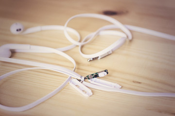 Broken white audio headphones cable lying on wooden surface