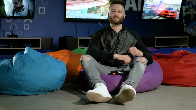 Man plays computer games with a joystick. Gamer sits on the meager chairs in the background of working televisions.
