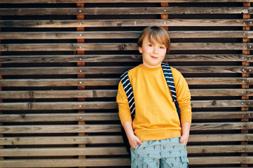 Outdoor portrait of cute kid boy wearing yellow sweatshirt and backpack. Back to school concept