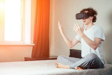 young man in virtual reality glasses on the bed in the bedroom. The concept of virtual reality and games