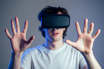 portrait of a young man in the glasses of virtual reality on a gray wall background. The concept of games in the mask of virtual reality