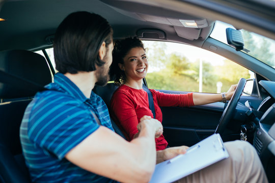 Driving school or test. Beautiful young woman learning how to drive car and handshaking with her instructor.