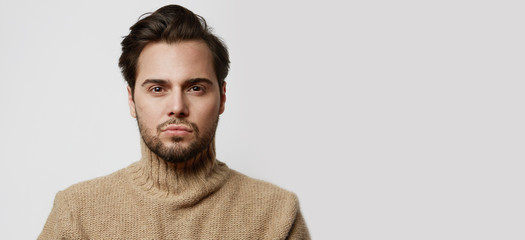 Young bearded fashion model in pullover jersey poising while standing on white background....