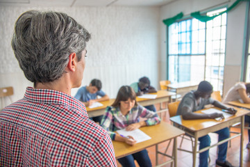 Teacher checking students doing school tests in a teenager classroom