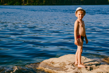 a boy stands on a big rock on the beach
