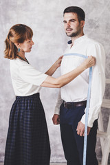 Woman tailor takes measures with male models. Fashion designer sews a costume for the model