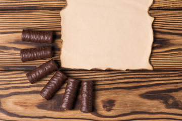Row of yummy chocolate candies near blank burnt paper on old weathered wooden table