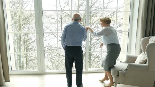 Senior couple at home, elderly husband looks at the window, his wife knits