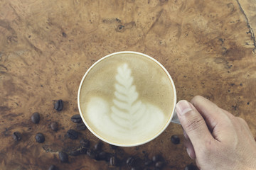 Hand hold a cup of coffee on wooden background, Top view.