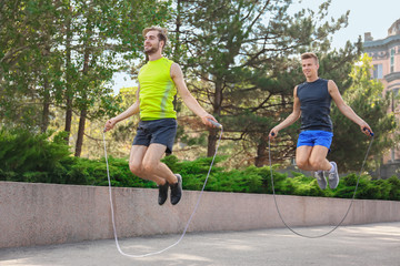 Young men in sportswear with jumping ropes in park