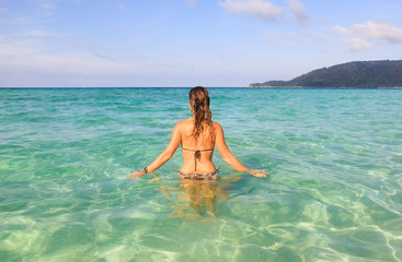 Woman in bikini slowly entering transparent turquoise water on a beach in Kecil, the smallest of Perhentian Islands, Malaysia.
