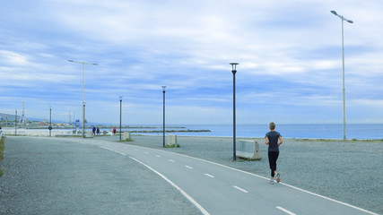 Fototapeta na wymiar Senior woman running in a promenade against a blue cloudy sky. Active ageing concept and empty copy space for Editor's text.