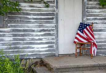 American flag draped over old wooden chair by rustic house door