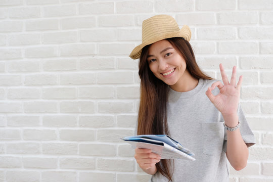 Young asian woman holding map and smiling with ok guster hand sign on white wall background with copy space, travel summer holiday vacation concept