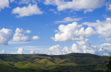 a simple landscape with green rolling hills and white puffy clouds against a clear blue sky