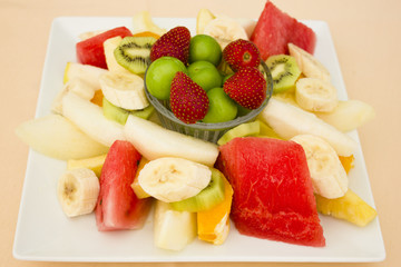 Fruits on a plate. Green plum, strawberry, banana, kiwi, watermelon, orange and apple.