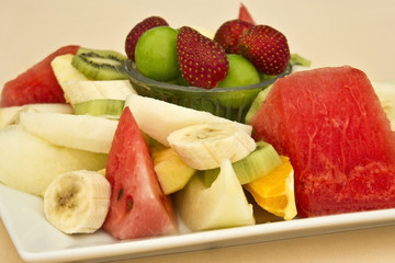 Fruits on a plate. Green plum, strawberry, banana, kiwi, watermelon, orange and apple.