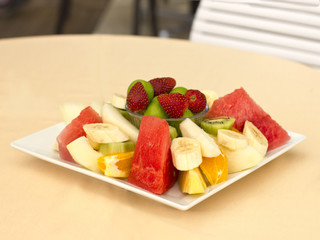 Fruits on a plate. Green plum, strawberry, banana, kiwi, watermelon, orange and apple.