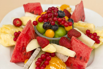 Fruits on a plate. Green plum, red currant, blueberry, strawberry, physalis, pitahaya, watermelon, orange and apple.