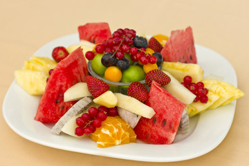Fruits on a plate. Green plum, red currant, blueberry, strawberry, physalis, pitahaya, watermelon, orange and apple.