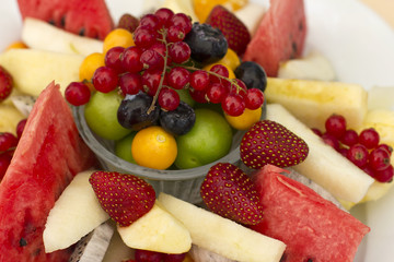 Fruits on a plate. Green plum, red currant, blueberry, strawberry, physalis, pitahaya, watermelon, orange and apple.