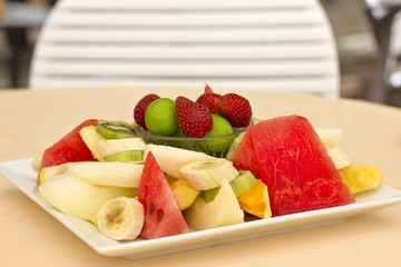 Fruits on a plate. Green plum, strawberry, banana, kiwi, watermelon, orange and apple.