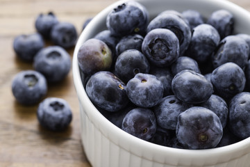 Small White Bowl filled with Blueberries, six blueberries on the left side, wooden background