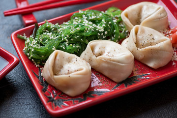 Close-up of steamed asian dumplings served with chuka salad on a red tray, selective focus