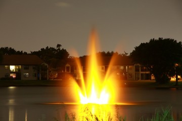 Yellow Golden Glowing Illuminated Fountain at Night on a Lake Overlooking a Residential Community with House Lights On