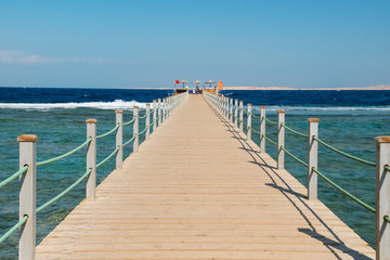 View of a wooden pier on the tropical seashore with blue sky and sea.