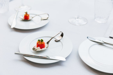 Modern French food: Diced watermelon with white crush cheese served in silver spoon on white plate with cutlery as appetizer.