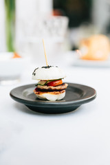 Modern French appetizer: Mini hamburger including white bun, pork, sliced cucumber, tomato and raddish topping with black sesame.