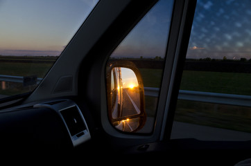Side rear-view mirror in the evening on the road during sunset