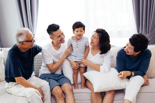 Happy Asian extended family sitting on sofa together, posing for group photos