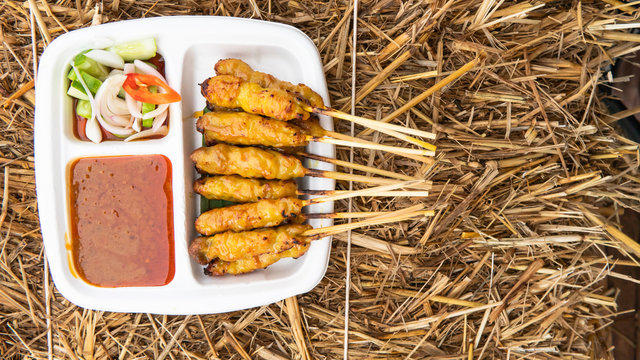Grilled pork skewing satay served with saurce and cucumber prickle. DIsk is on the hay-made table.