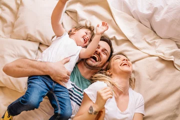 Fotobehang Happy family having fun in the bedroom while they lie on bed © Nebojsa