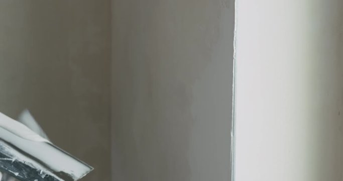 Slow motion pan of worker applying putty on the wall near window