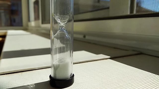 hourglass with a fleeting white sand inside, stand on a window sill, time lapse