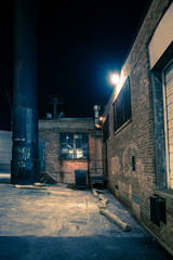 Dark and eerie urban city alley with vintage warehouses and factory buildings at night