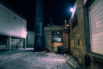Dark and eerie urban city alley with vintage warehouses and factory buildings at night
