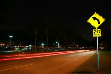 Yellow Speed Limit 20 Mph Sign in a Residential Neighborhood at Night with Car Lights Streaking by...
