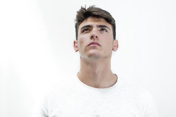 Retrato de hombre joven atractivo mirando hacia arriba con camiseta blanca sobre fondo blanco