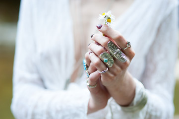 A hippie girl in ornaments of the Boh chic dressed in lace clothes is holding a daisy flower