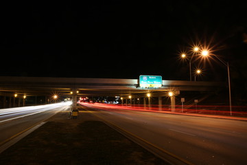 Traffic Traveling East and West along Sample Road in Pompano Beach at Night under the I-95 Overpass with North to West Palm Beach Sign