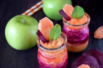 Layered smoothie with beet, carrot and apple in glass jars