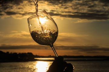 Female hand with a glass of white wine on the background of a beautiful sunset.  Travel vacations concept.