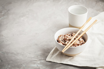 Assorted multi-colored wild rice in ceramic bowl and chopsticks with goblet of water. Black, brown and white rice...