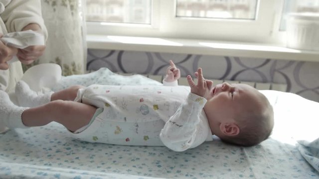 Adorable newborn baby crying while his mother dressing him