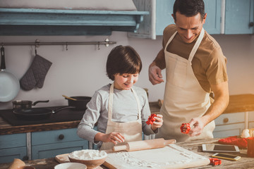 Content father and his son making biscuits. They holding cookies cutters and smiling. Copy space in left side
