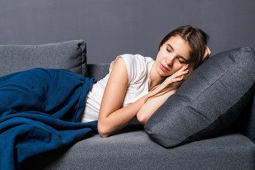 Portrait of a young cute girl sleeping on the sofa in light livingroom. Her head is on grey pillow...